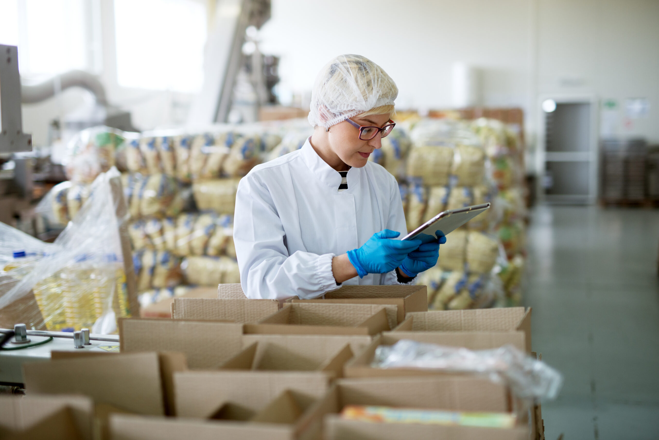 Worker inspecting boxes with food products in lab apparel and notepad